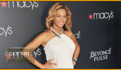 Woman posing at an event with a banner reading "macy's" and "beyoncé pulse." she wears a white dress and smiles confidently.