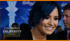 Woman with blue hair smiling at an event with a “celebrity gps” watermark and a promotional background.